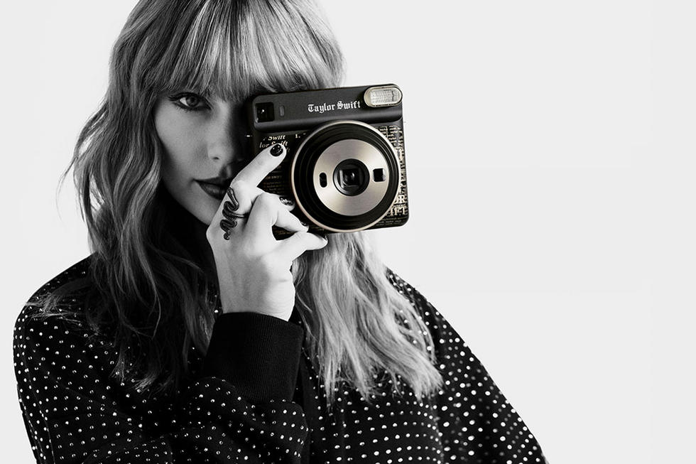 A black-and-white image of Taylor Swift taking a picture with a Fujifilm Instax camera.