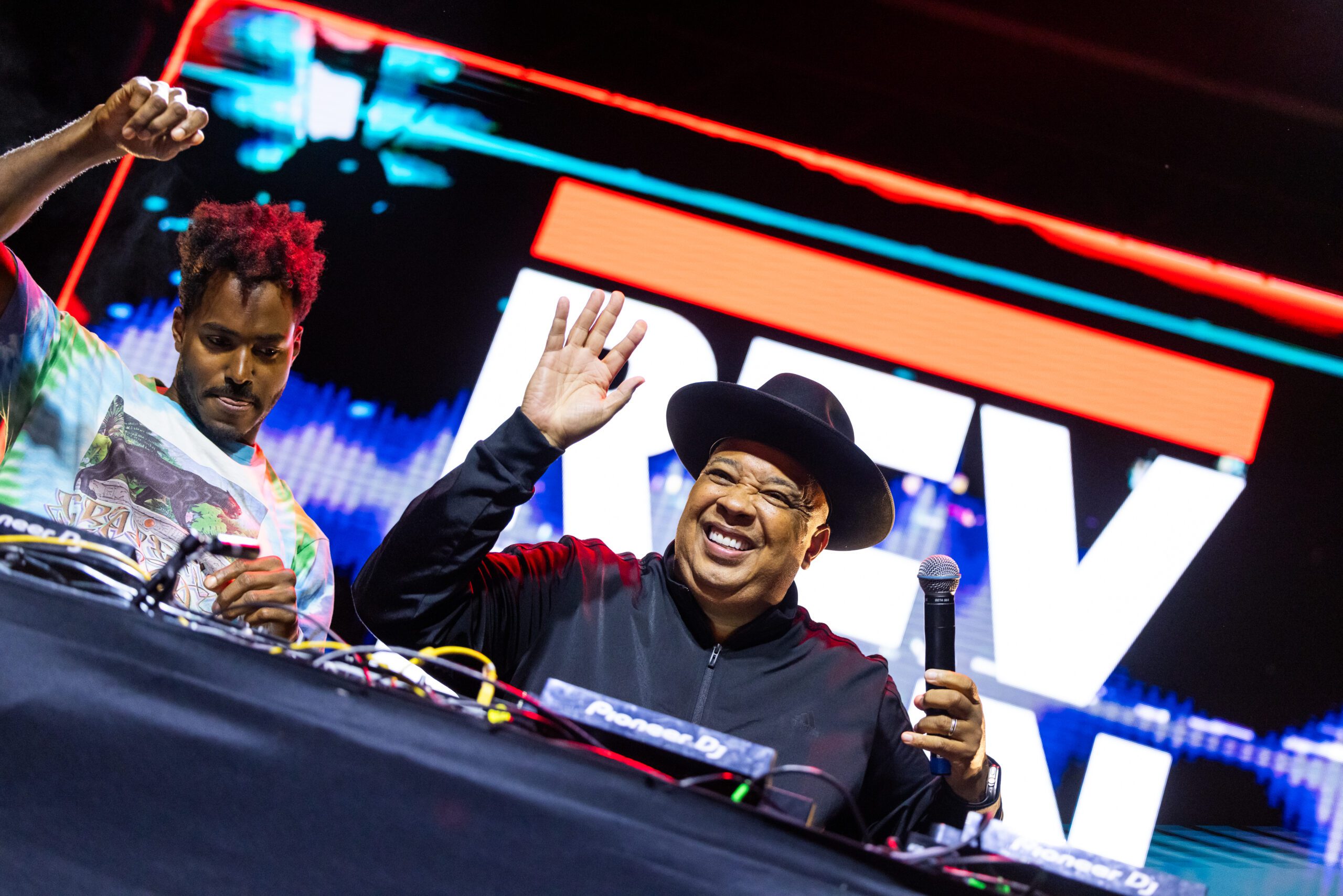 A performer and Joseph Simmons (a.k.a. Rev. Run) wave to the crowd while holding a mic.